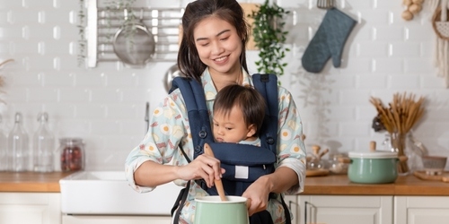 Seorang ibu sedang memasak sambil menggendong bayi